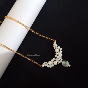 A golden chain necklace with a crescent-shaped cluster of white pearls. A single, large iridescent bead hangs at the bottom of the pearl cluster.